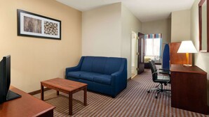 Een hotelkamer met een blauwe bank, een houten tafel, een bureau met een lamp en een lijst met een afbeelding aan de muur.
