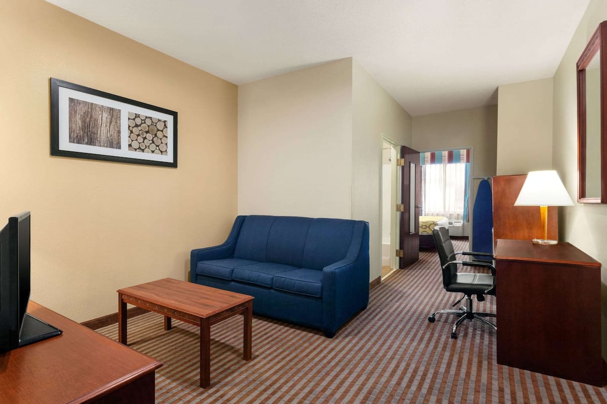 A hotel room with a blue sofa, a wooden table, a desk with a lamp, and a framed picture on the wall.