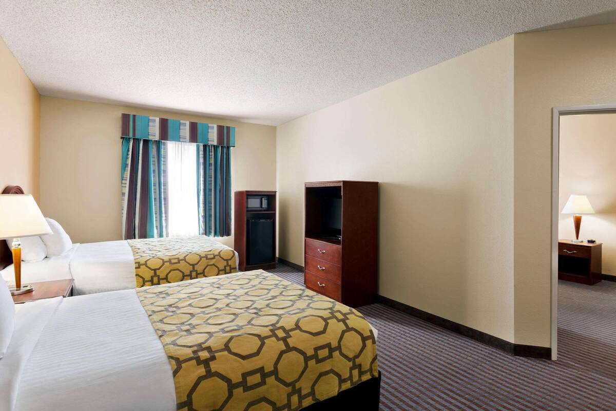 A hotel room with two beds, a TV, a wardrobe, and a desk with a lamp.