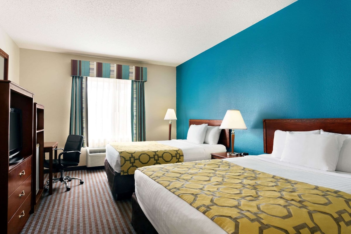 A hotel room with two beds, a desk, a chair, a TV, and a wardrobe.