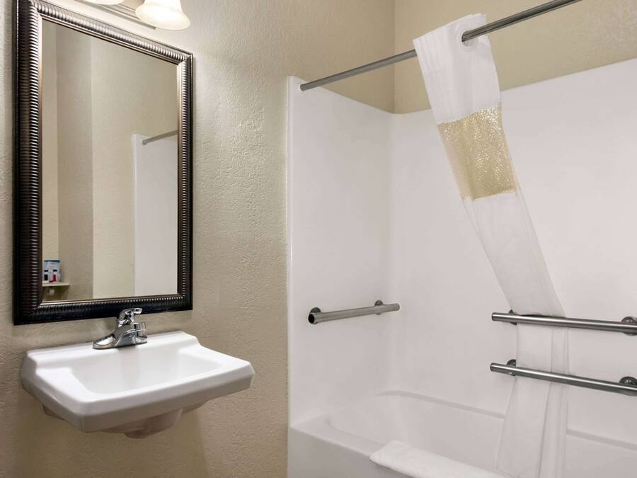 A bathroom with a white sink, a mirror, and a shower with grab bars.