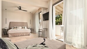 A modern bedroom with a large bed, a ceiling fan, a TV, and a balcony with sheer curtains. - Ino Hotel & Suites (Samos)