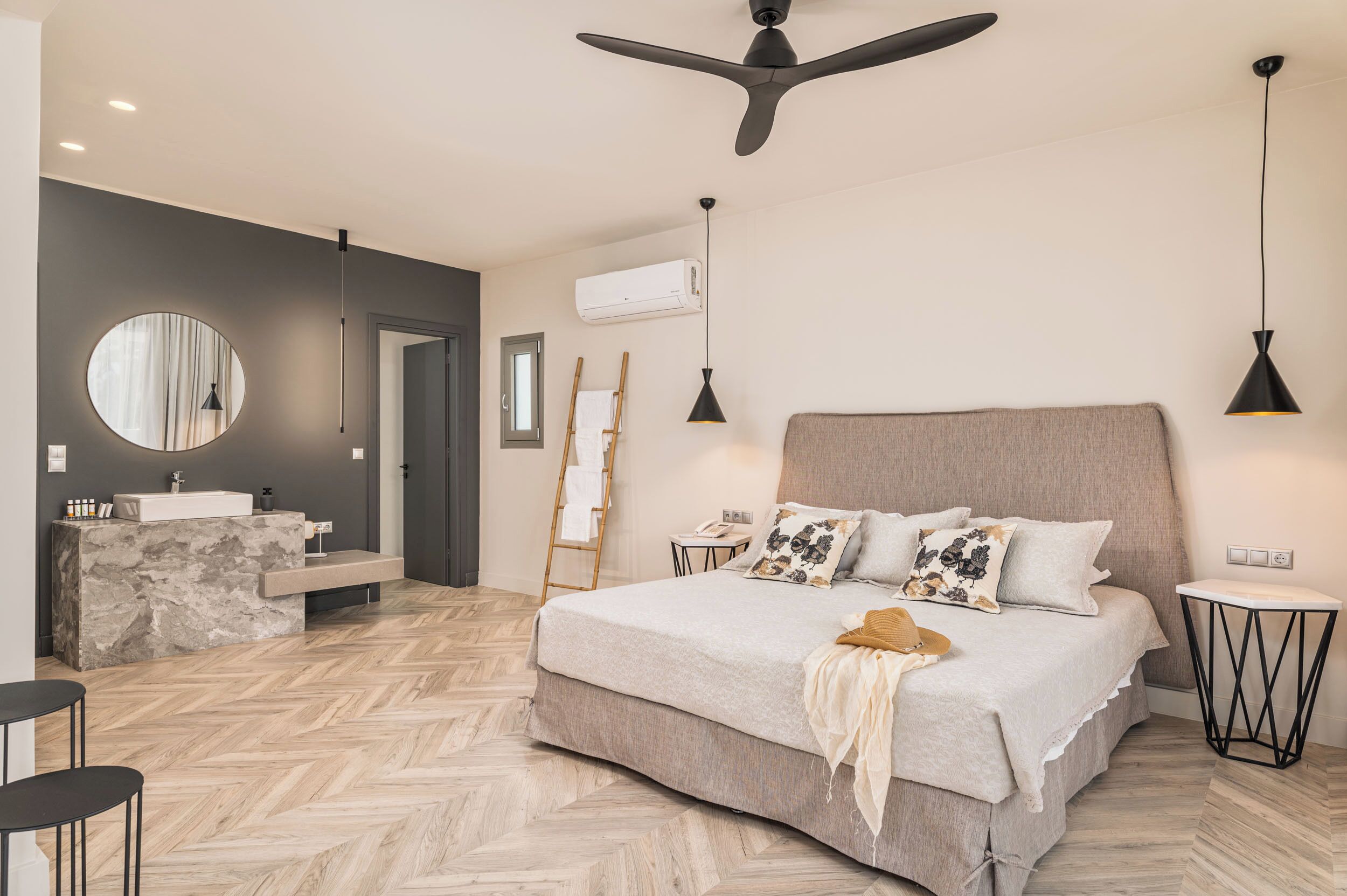 A modern bedroom with a large bed, a vanity with a mirror, and a herringbone-patterned floor.