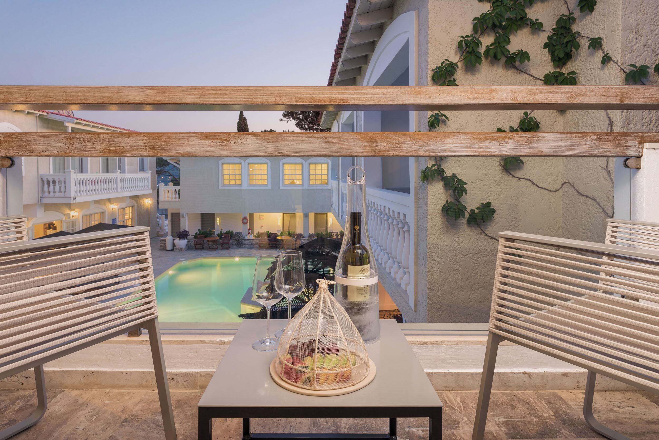 Une terrasse avec une piscine, une table avec une bouteille et des verres, et un banc.