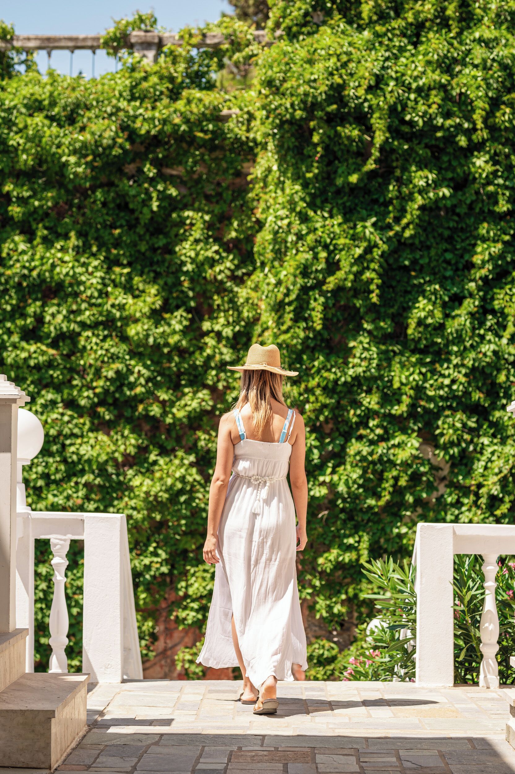 A woman in a white dress and straw hat walking on a stone pathway.