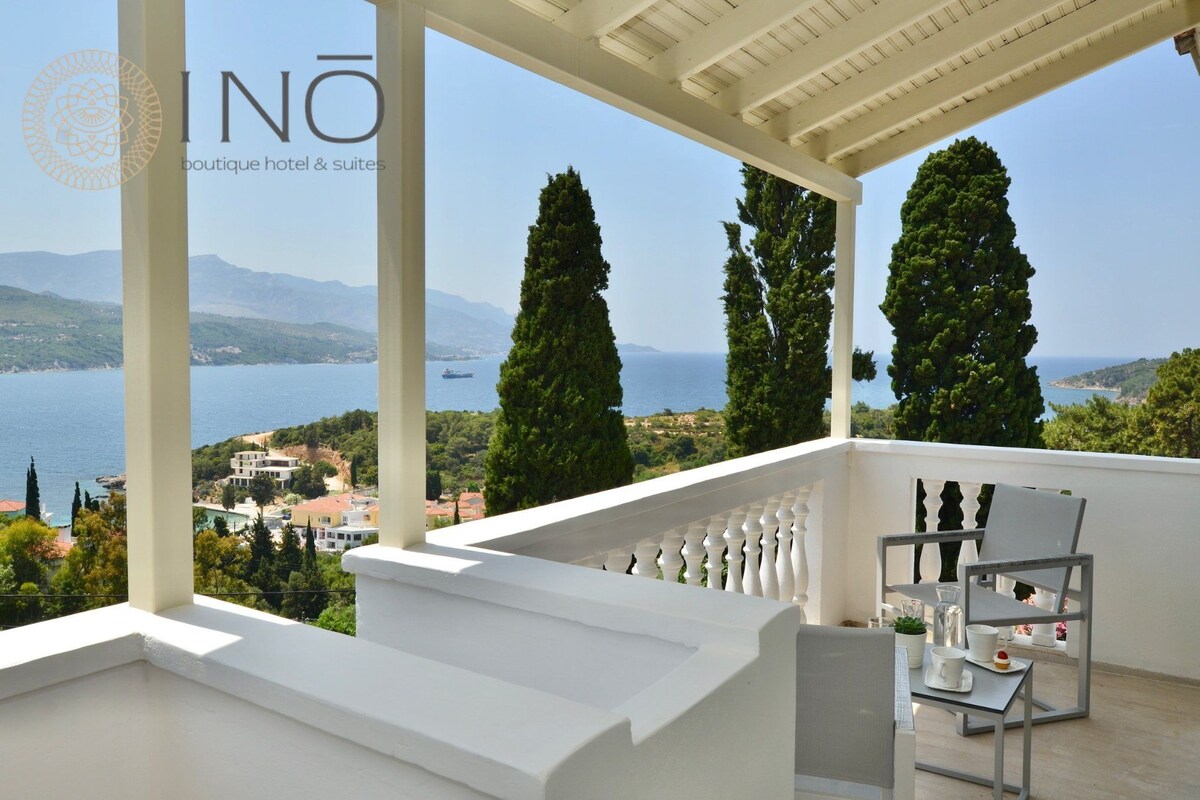 A balcony with a view of the sea, white balustrades, and a table with chairs.
