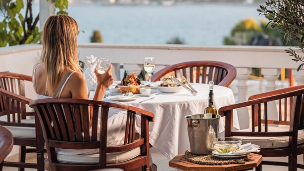 A terrace with a table set for two, overlooking a body of water and hills. - Ino Hotel & Suites (Samos)