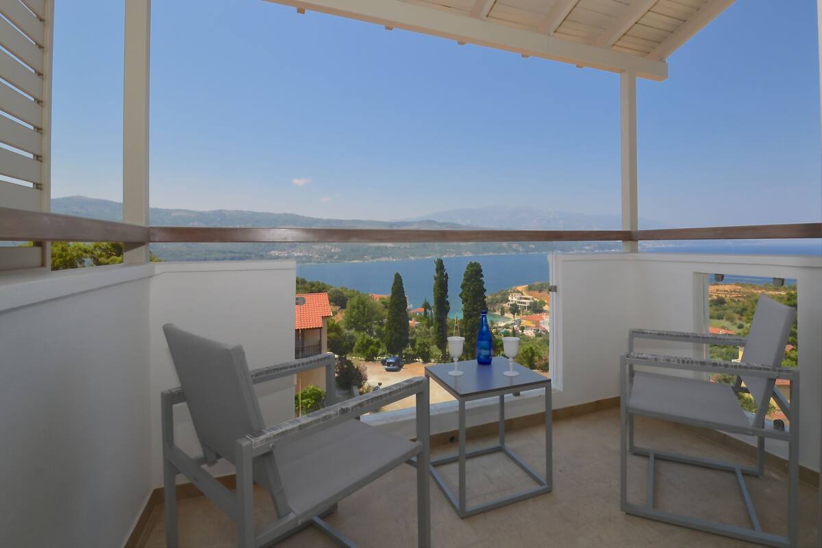 Un balcón con dos sillas y una mesa, con vista a un paisaje pintoresco de un lago y montañas a lo lejos.