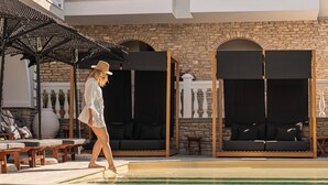 A poolside area with lounge chairs, a covered seating area, and a stone wall backdrop. - Ino Hotel & Suites (Samos)