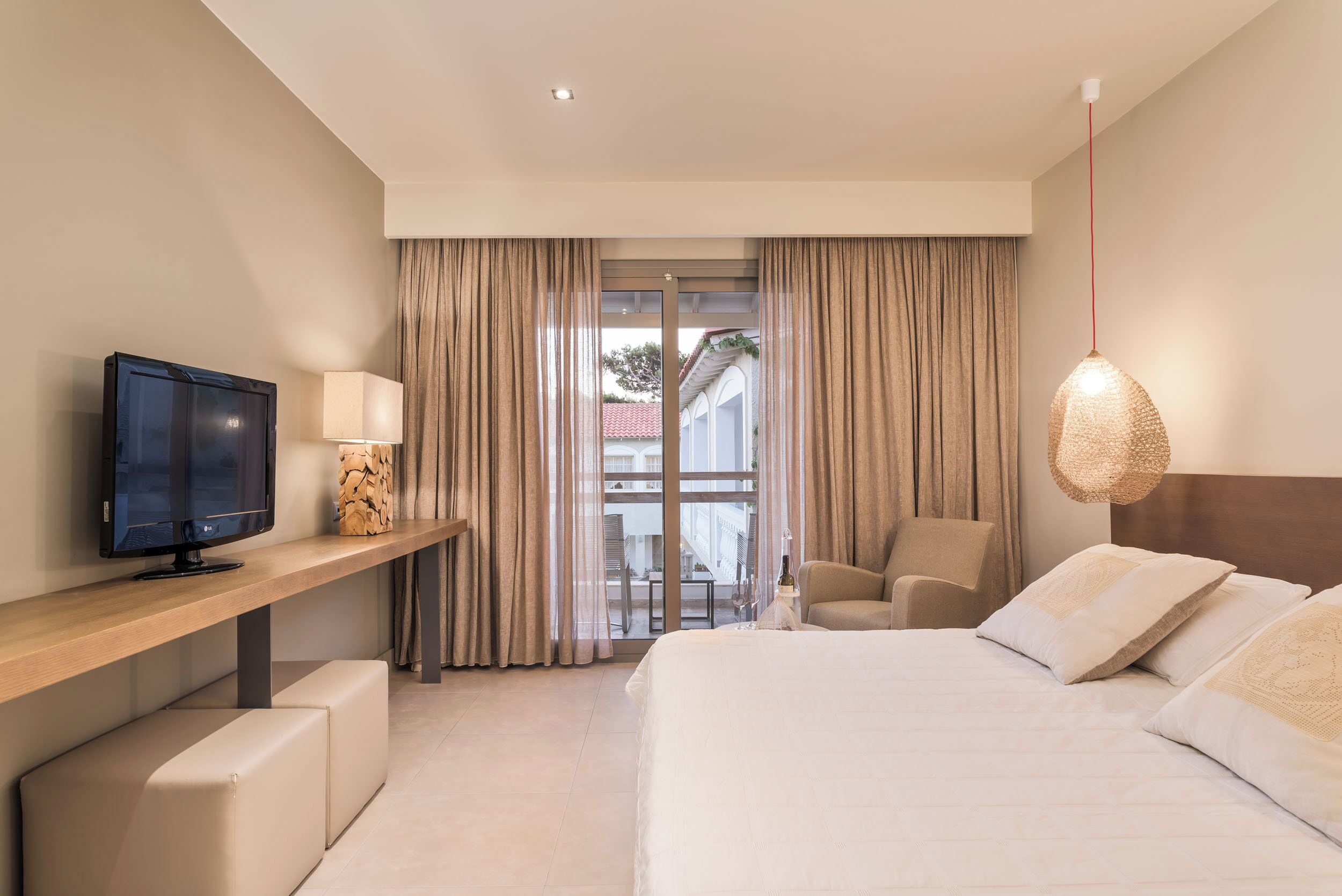 A modern hotel room with a large bed, a TV on a wooden console, a chair, and a balcony view.