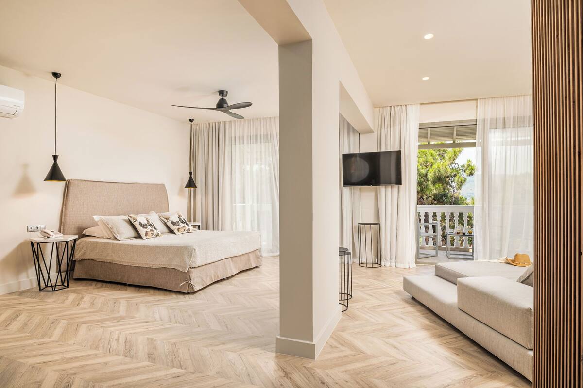 Un dormitorio moderno con cama, sofá, televisión y balcón con vistas.