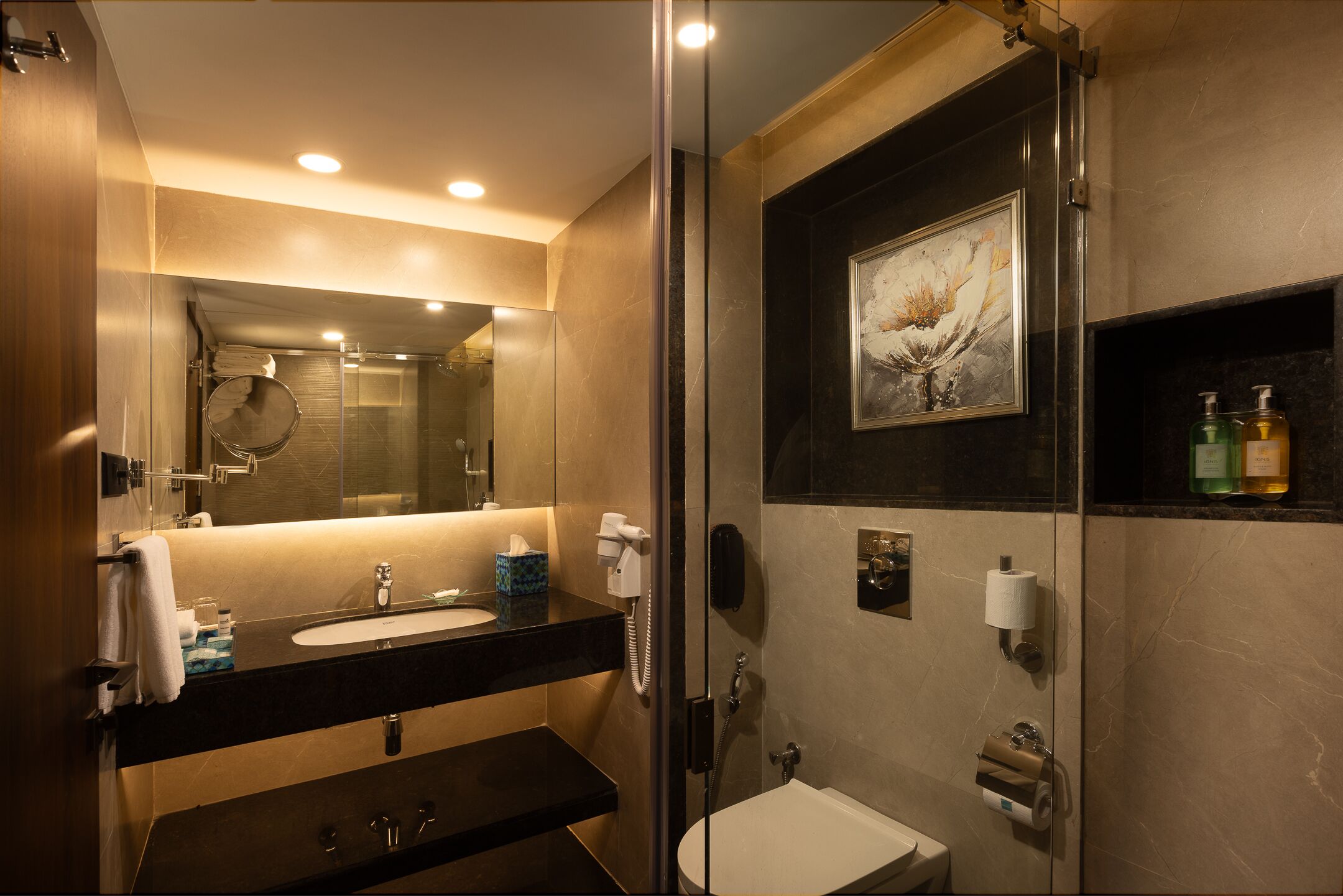Une salle de bain moderne avec une douche à parois de verre, un grand miroir et un lavabo agrémenté d’articles de toilette.