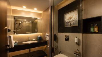 Une salle de bain moderne avec une douche à parois de verre, un grand miroir et un lavabo agrémenté d’articles de toilette.