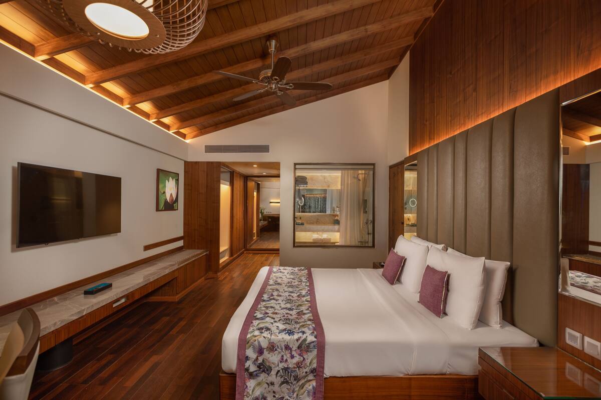 A modern hotel room with a large bed, wooden ceiling, a flat-screen TV, and a bench.