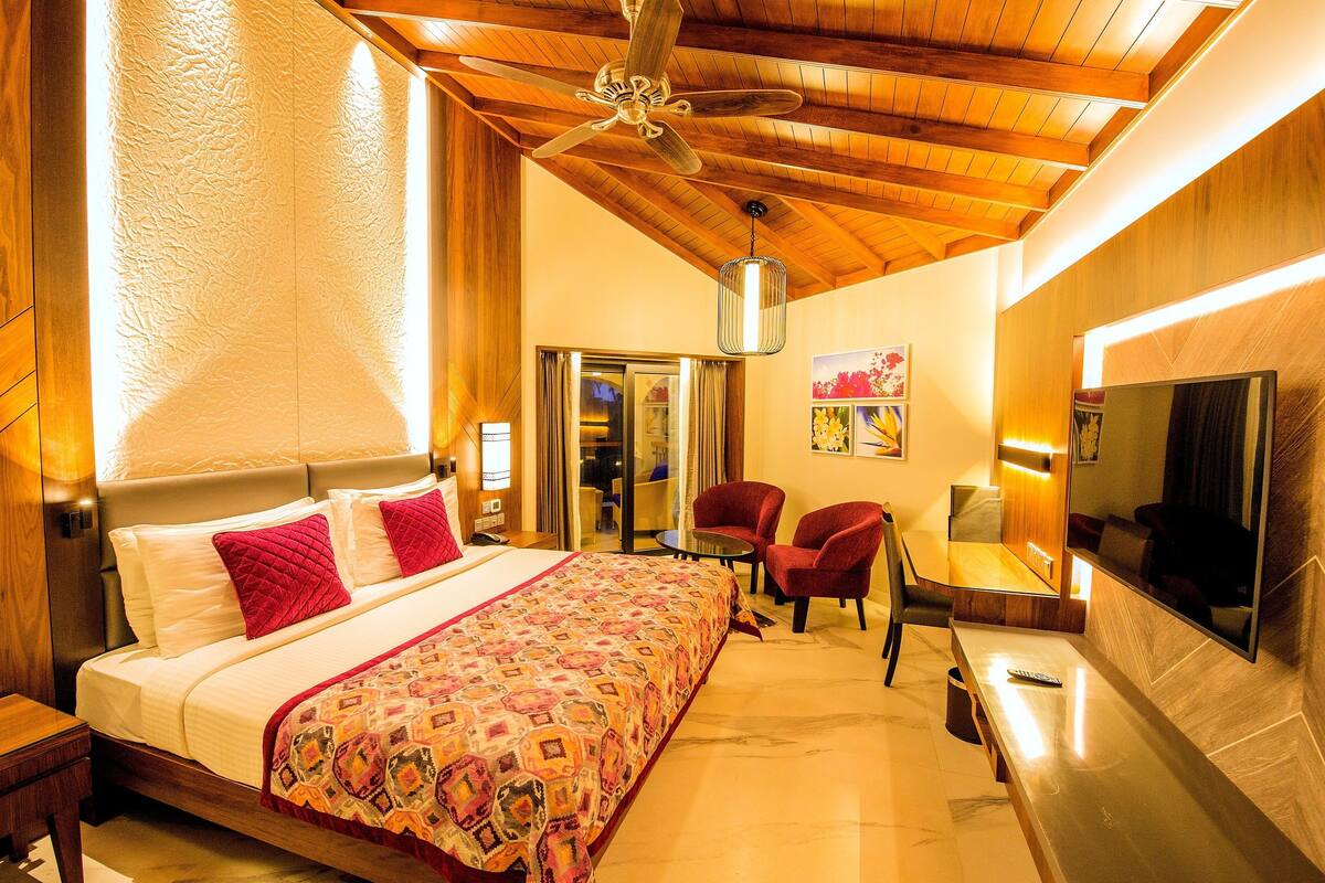 A hotel room with a large bed, a desk, a chair, a ceiling fan, and a TV.