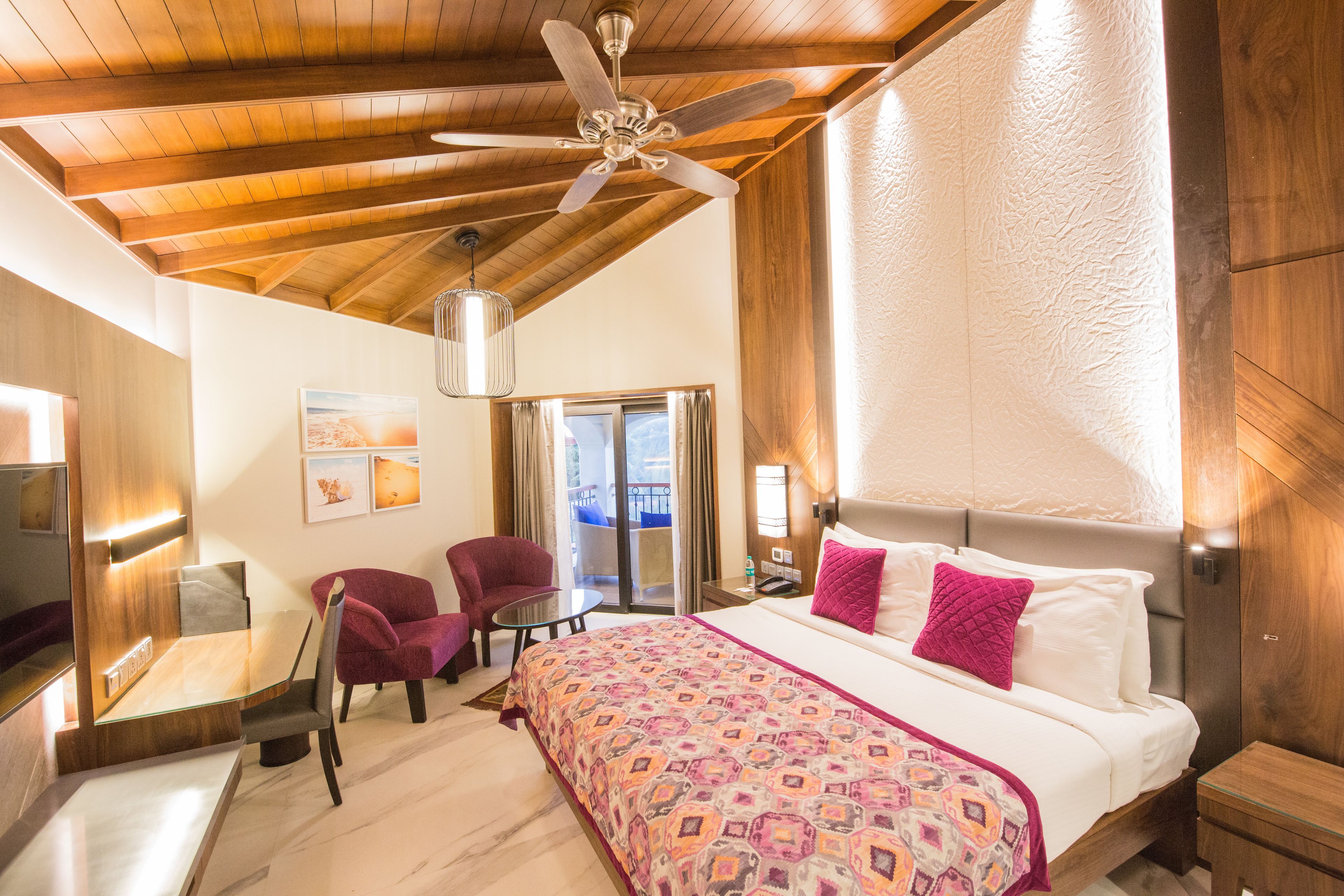 Une chambre d’hôtel avec un plafond en bois, un lit recouvert d’une couvre-lit à motifs, un bureau avec une chaise et une vue sur l’extérieur grâce à une porte coulissante.