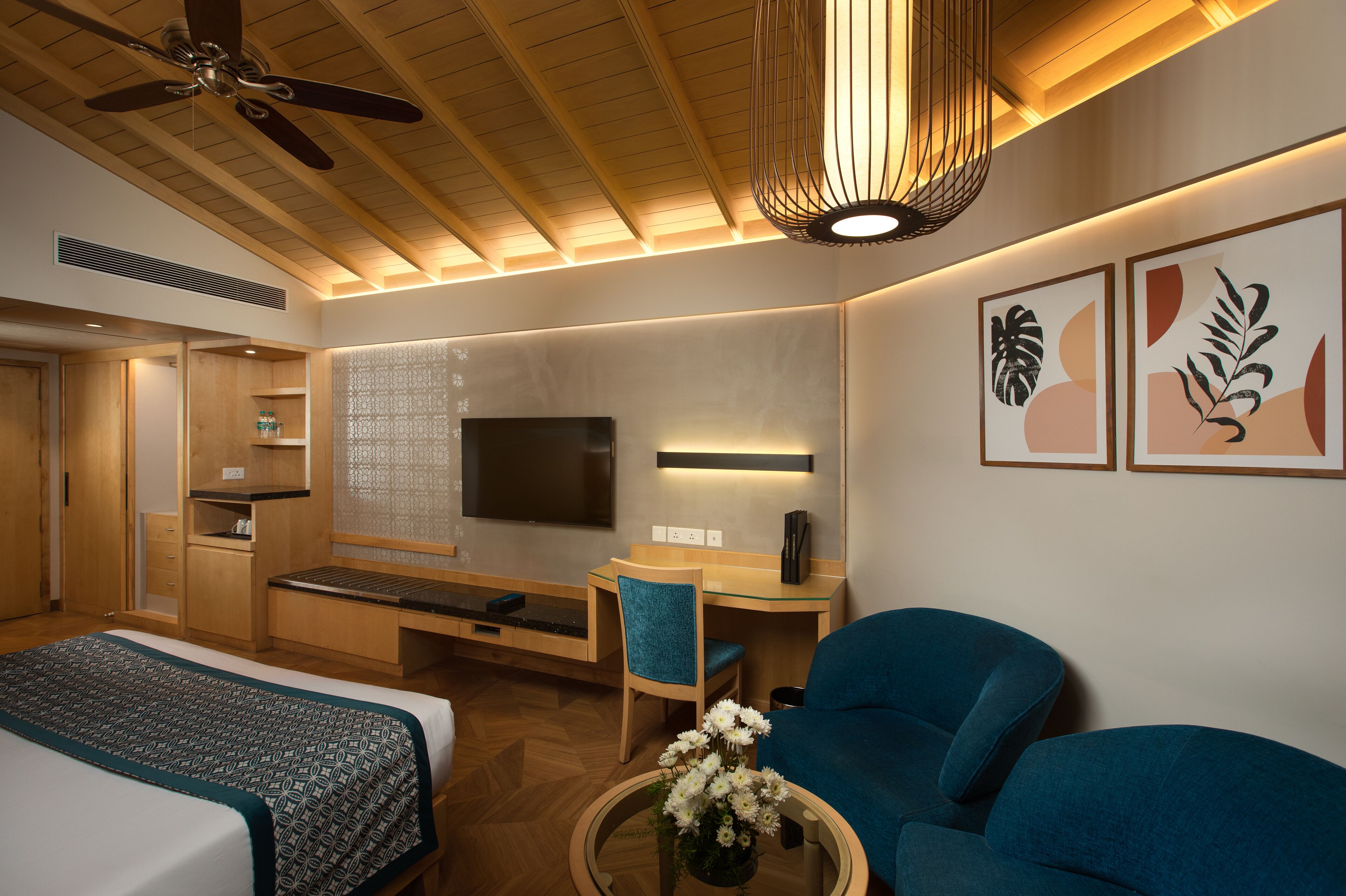 A hotel room with a bed, a desk, a chair, a TV, and artwork on the wall.