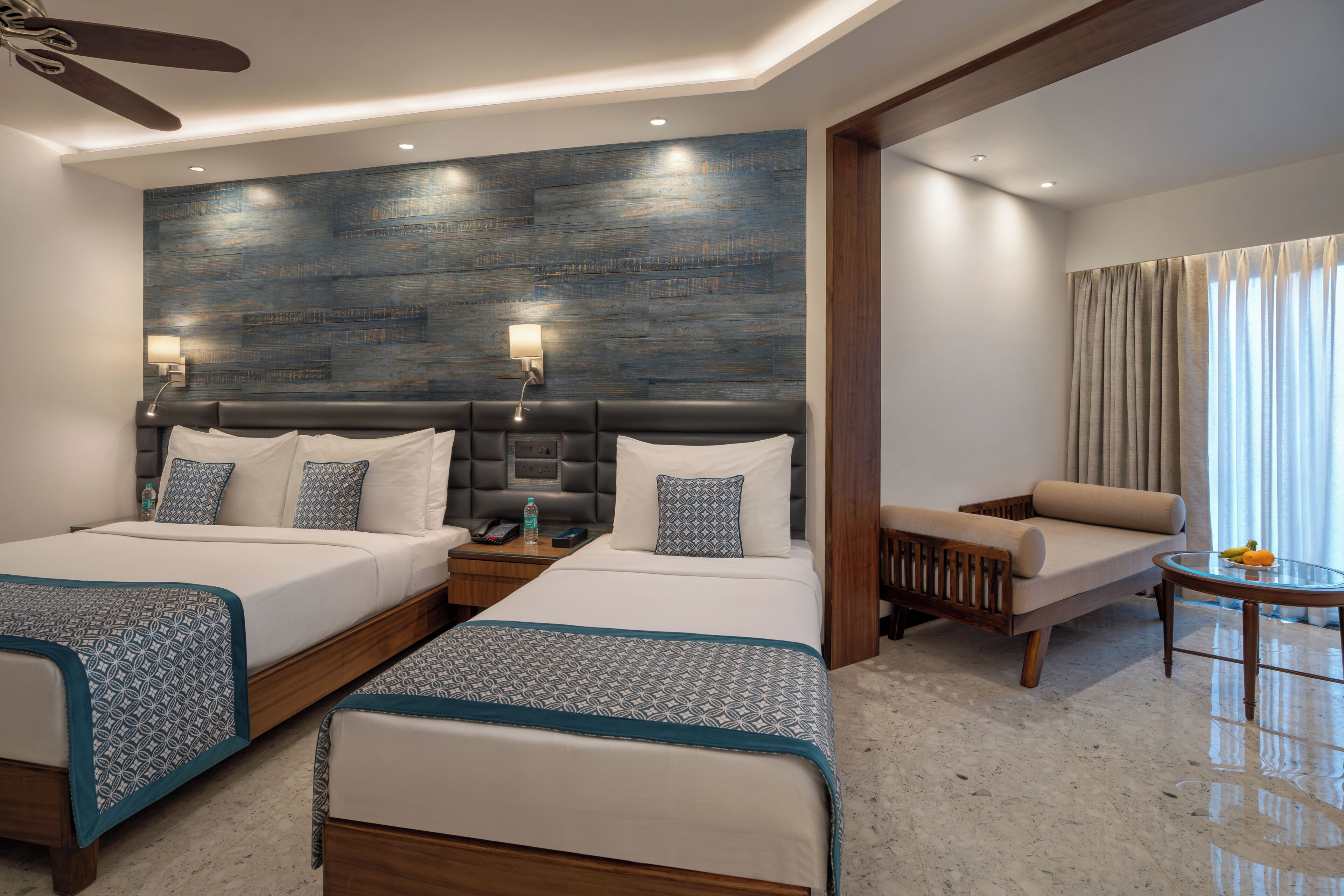 A hotel room with two beds, a sofa, a small table, and a ceiling fan.