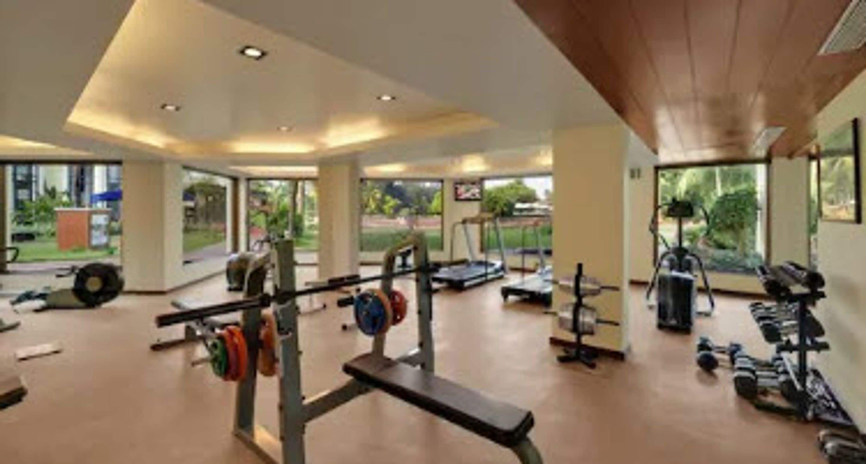 A spacious gym with various exercise equipment, large windows, and a view of the outdoors.