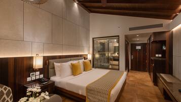 Quarto de hotel moderno com uma cama grande, mesas de cabeceira, uma escrivaninha e um banheiro visível através de uma porta de vidro.