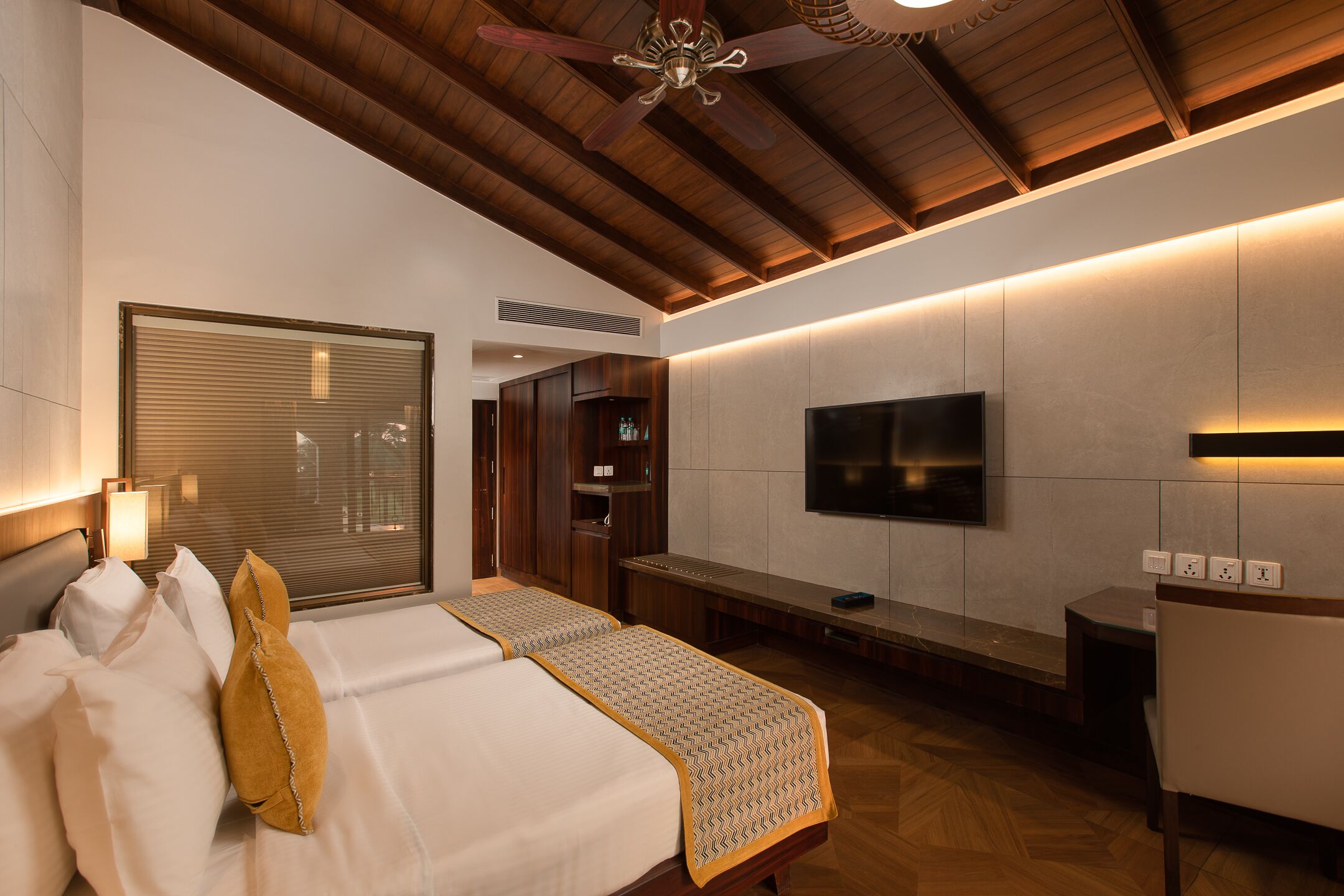 A hotel room with a large bed, a bench, a TV, and a ceiling fan.