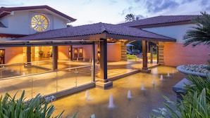 Entrada de un hotel con un corredor cubierto, un ventanal circular grande y una fuente.