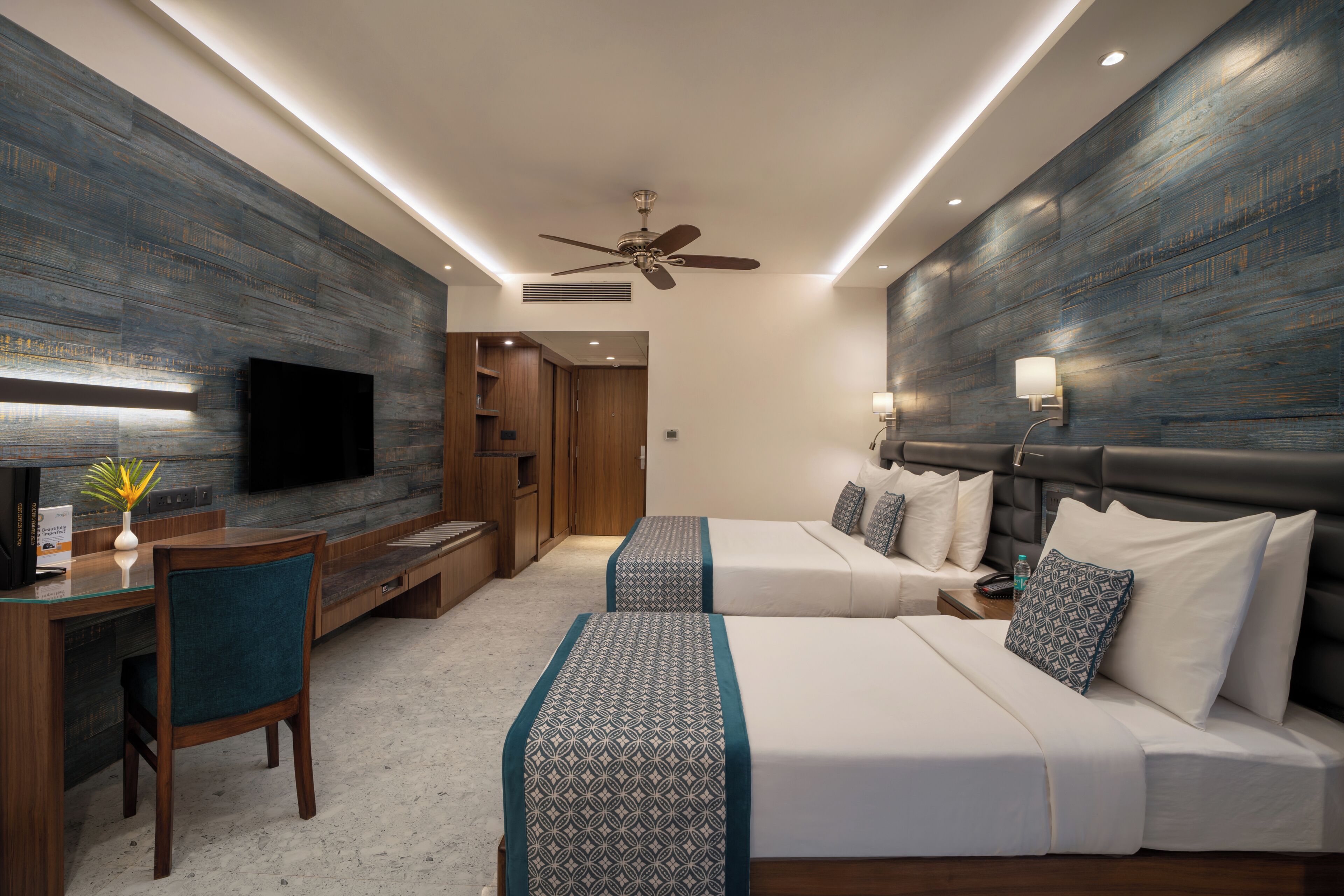 A hotel room with a TV, desk, two beds, and a ceiling fan.