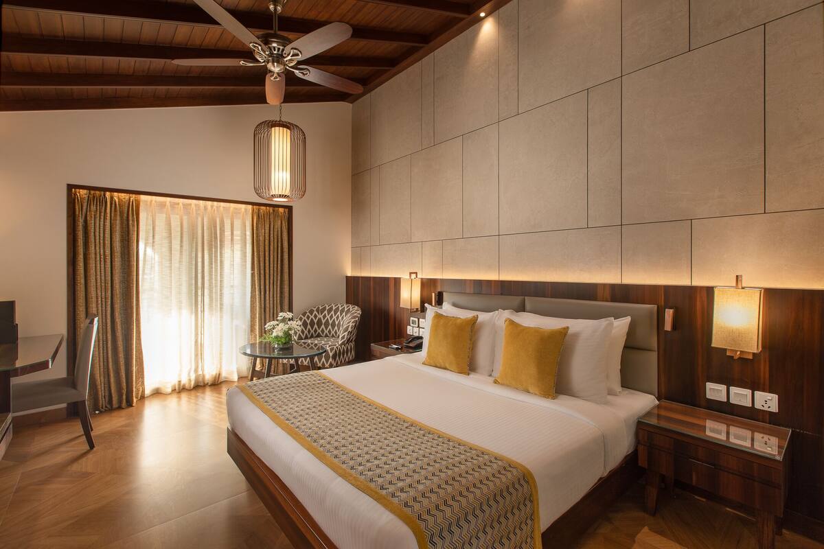 A hotel room with a large bed, a desk, a chair, and a ceiling fan.
