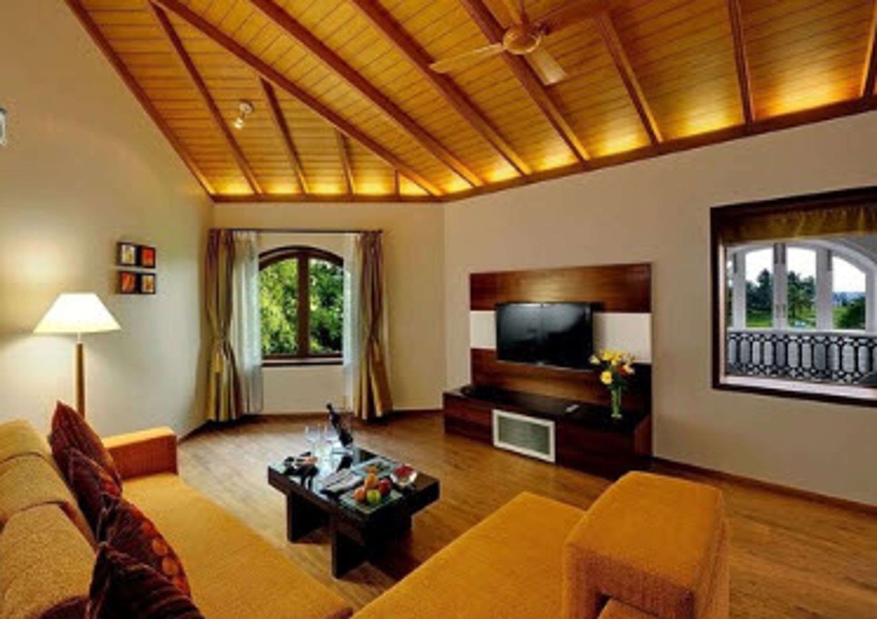 Un soggiorno con soffitto in legno, una televisione su un mobile in legno, un divano, un tavolino da caffè con della frutta e una finestra con tende.