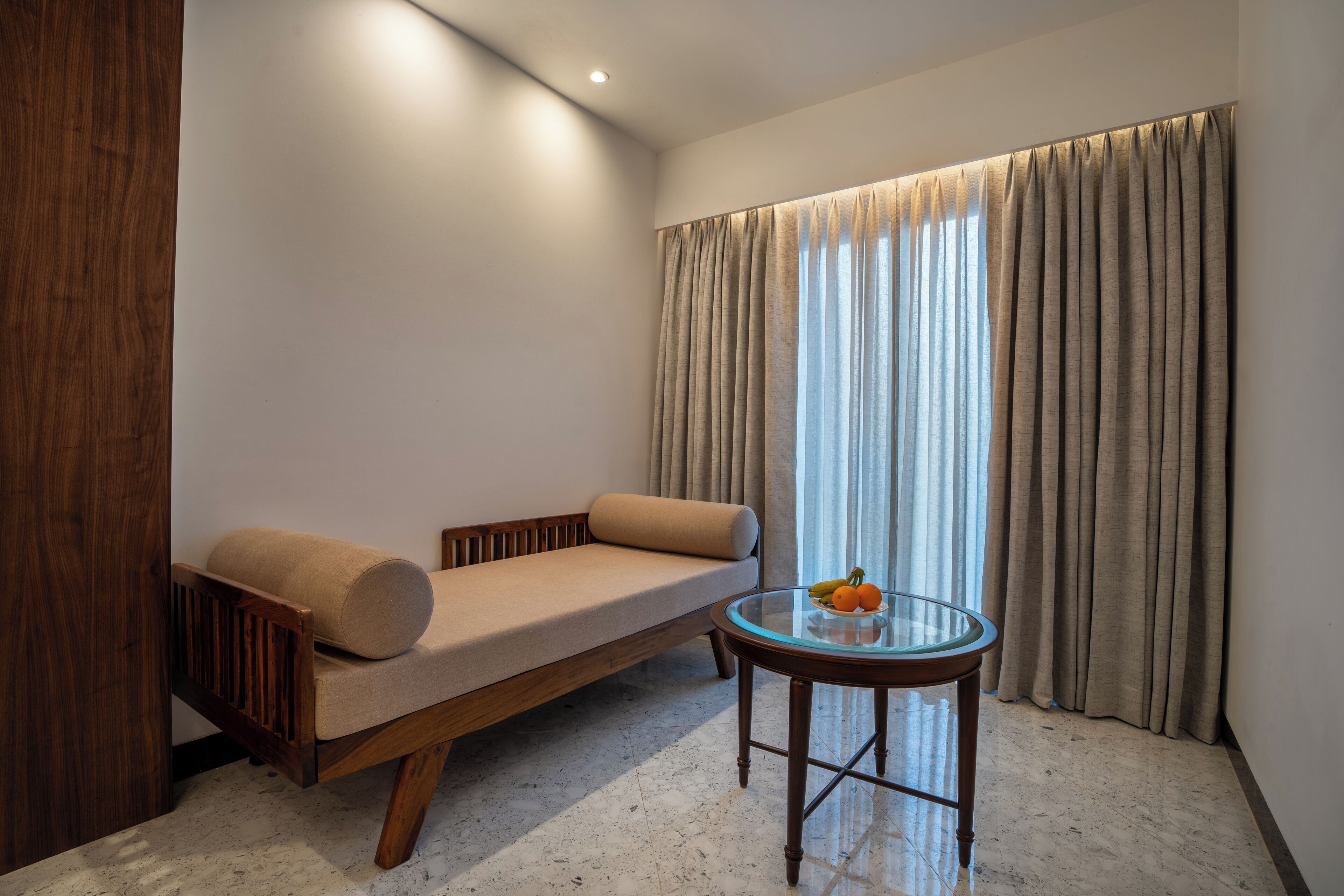 A modern room with a sofa, a glass table with fruit, and a window with curtains.