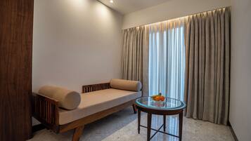 A modern room with a sofa, a glass table with fruit, and a window with curtains.