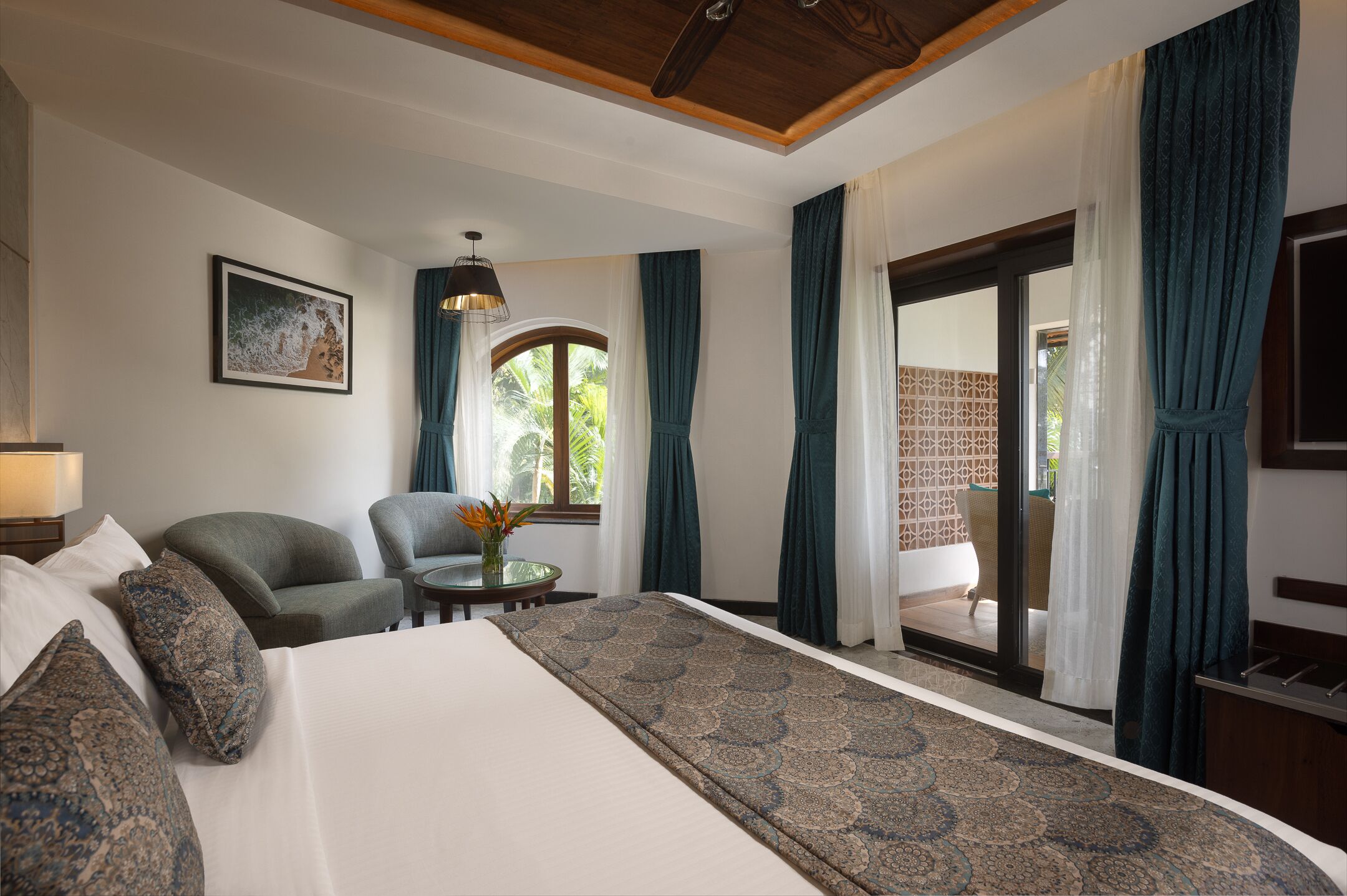 Habitación de hotel con una cama grande, dos sillones, una mesita con un florero y vistas al exterior a través de un ventanal.