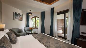 Habitación de hotel con una cama grande, dos sillones, una mesita con un florero y vistas al exterior a través de un ventanal.