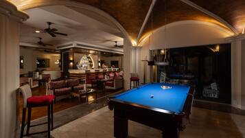 Una mesa de billar en una sala bien iluminada, con zona de bar y asientos.