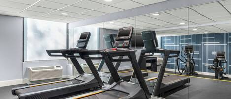 Un gimnasio con cintas de correr, bicicletas estáticas y un espejo grande.