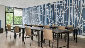 Una sala de conferencias con diseño moderno, que presenta un muro con patrón geométrico, varias mesas y sillas dispuestas para reuniones.