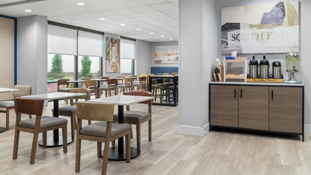 Un comedor moderno con mesas y sillas, una estación de café y ventanas amplias con vistas.