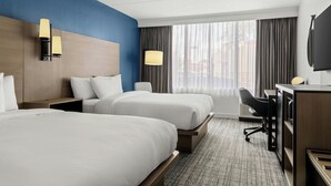 Habitación de hotel con dos camas, un escritorio, una silla y un televisor.