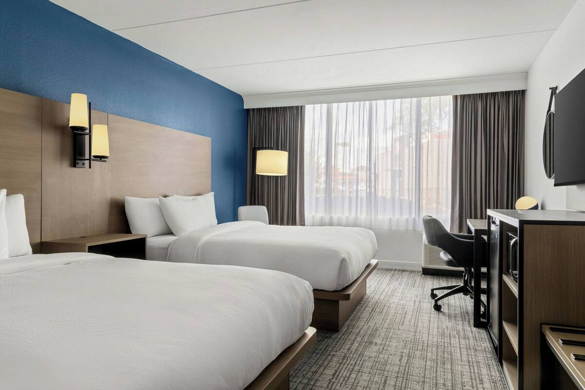A hotel room with two beds, a desk, a chair, and a TV.