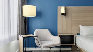 A hotel room with a bed, a chair, a bedside table, a lamp, and a wardrobe.