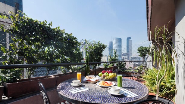 Una mesa redonda con una cubierta de mosaico azul, rodeada de sillas, en un balcón con vista a la ciudad.