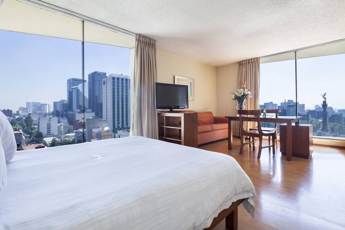 Une chambre d  ’hôtel avec un grand lit, un bureau, une chaise, une télévision et une vue sur le paysage urbain.