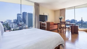 Habitación de hotel con una cama grande, un escritorio, una silla, un televisor y vistas a la ciudad.