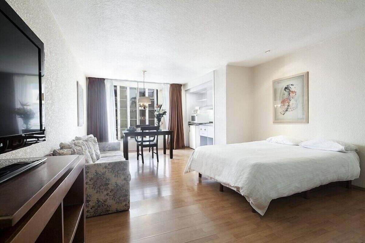 Une chambre d’hôtel comprenant un lit, un bureau avec un ordinateur, une télévision et un coin repas avec une table et des chaises.