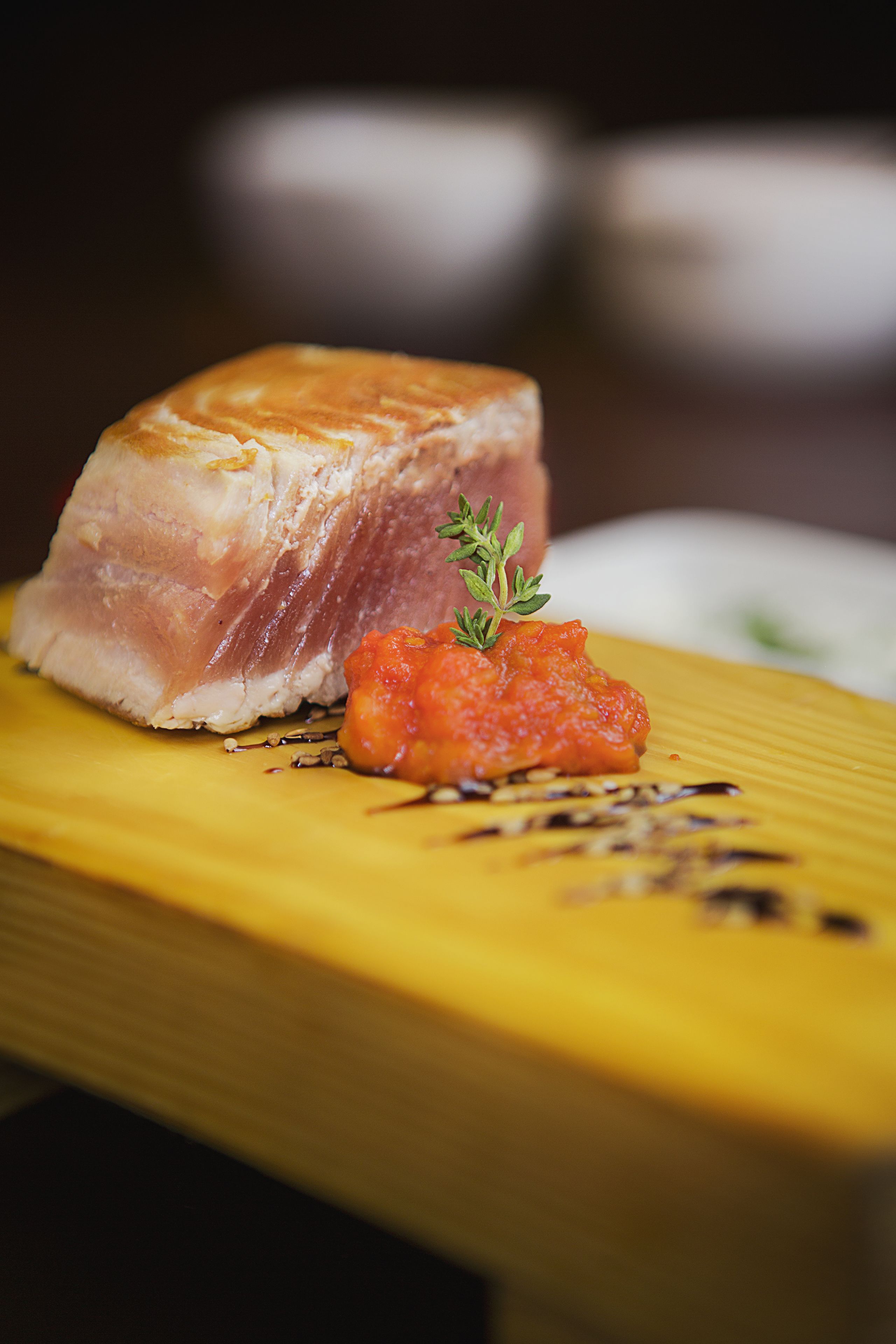 A wooden table with a piece of meat and a small portion of red sauce.