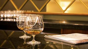 Two empty wine glasses on a reflective surface with a magazine and a triangular wall design in the background.
