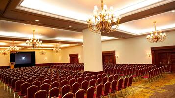 A conference room with rows of red chairs, a large screen, and chandeliers.
