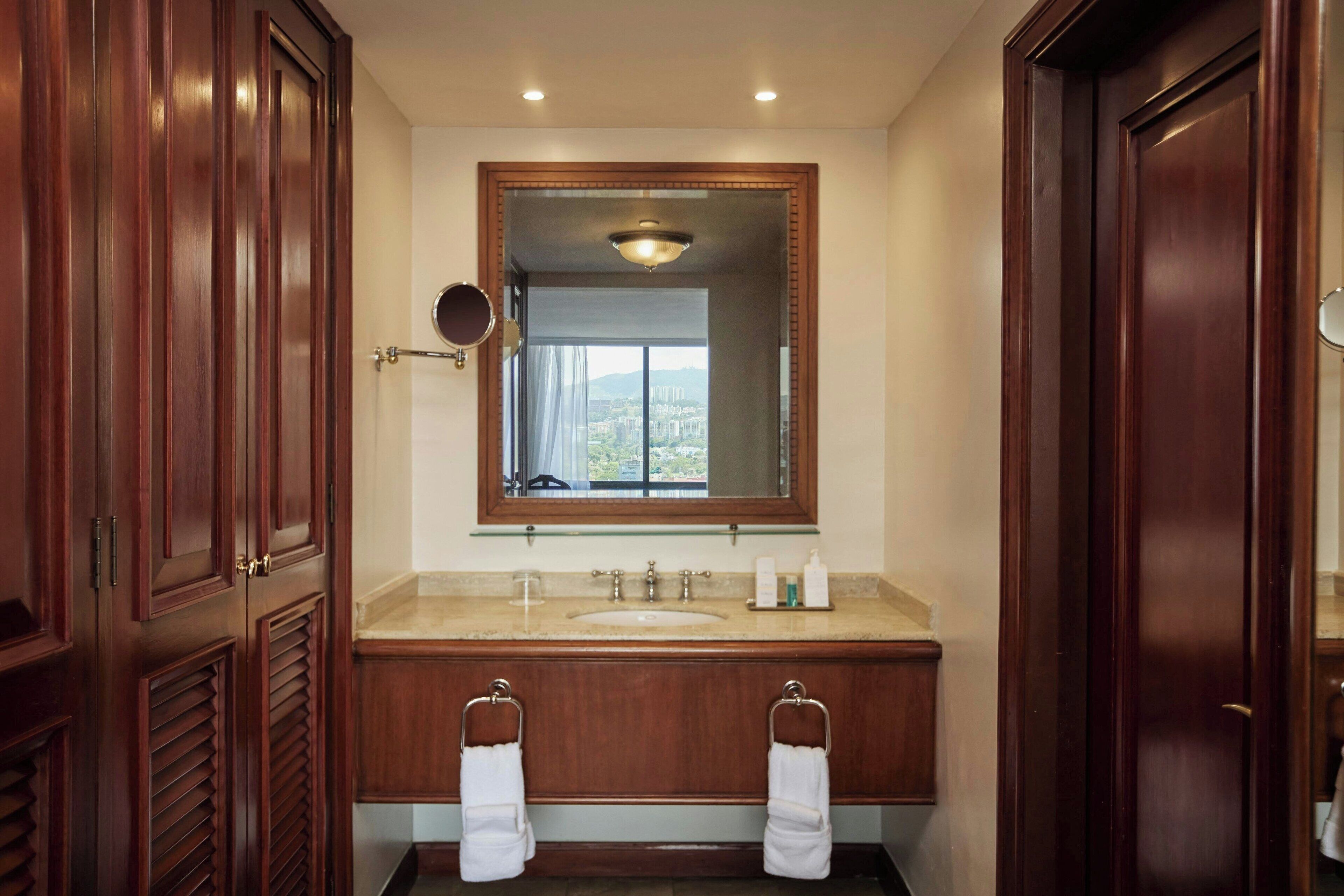 A bathroom with a wooden vanity, a large mirror, and a view of a cityscape through the window.