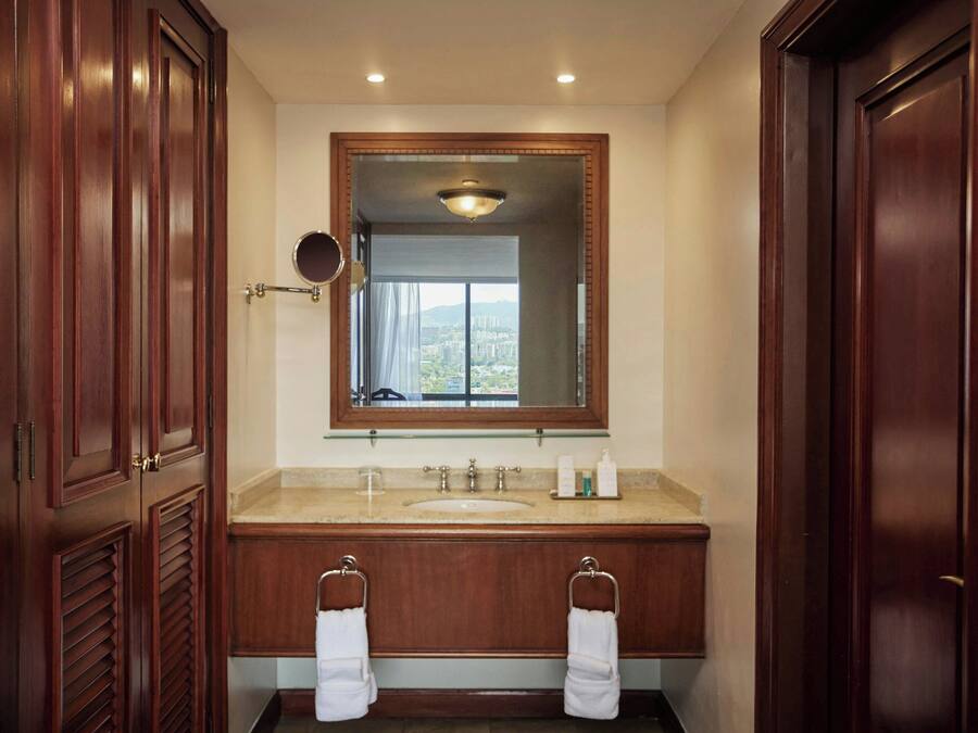 Un baño con tocador de madera, un espejo grande y vistas de la ciudad a través del ventanal.