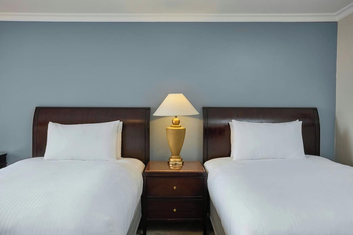 Una habitación de hotel con dos camas, una mesita de noche con lámpara y un aparador.